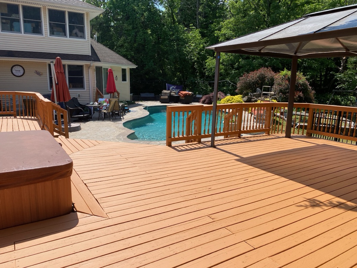 Stained poolside deck with hot tub and pergola by J&B Painting