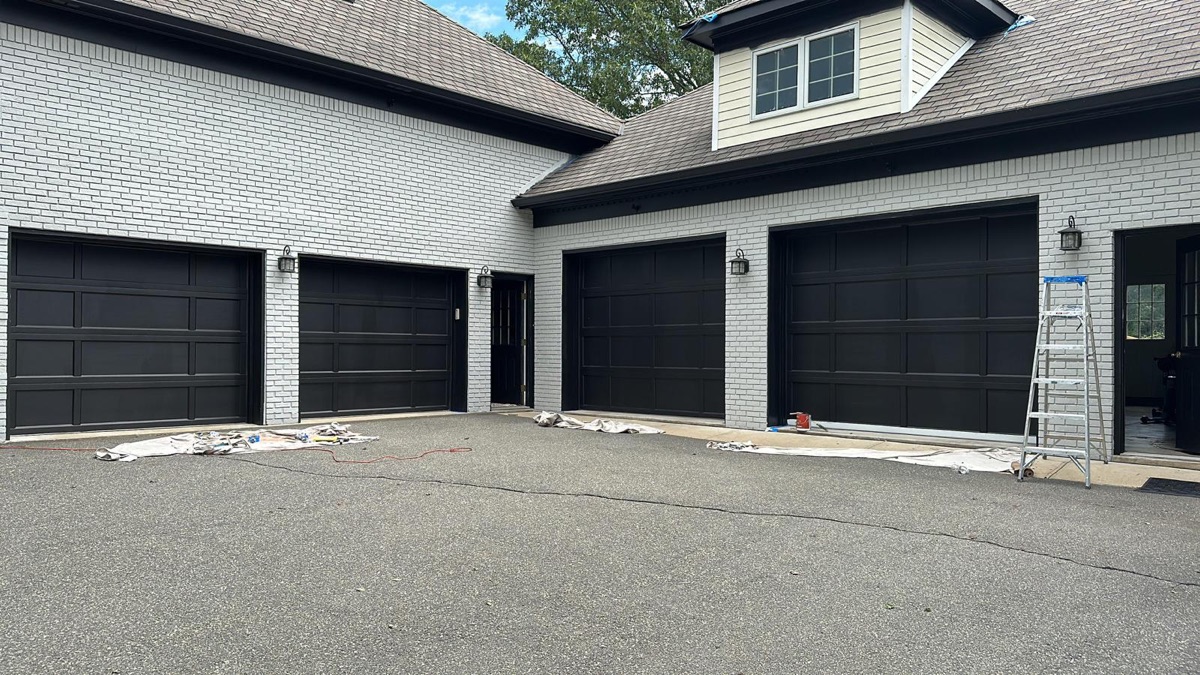 White painted brick home with black garage doors by J&B Painting